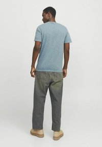 Lyseblå, kortærmet t-shirt med en blød tekstur, parret med løstsiddende grå jeans og beige fodtøj, set fra ryggen.