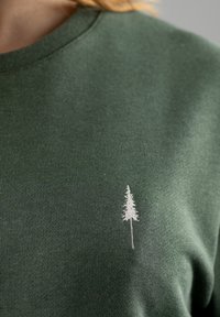 Groene katoenen t-shirt met een ronde hals en ribbeltextuur, voorzien van een kleine witte geborduurde boom aan de linkerkant.