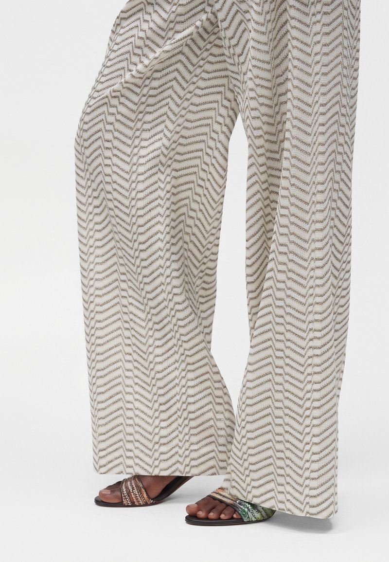 Pantalon à jambes larges avec motif zigzag beige et gris porté avec des sandales ouvertes à brides multicolores.