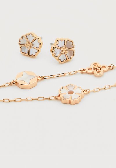 Σκουλαρίκια καρφωτά με λουλουδάτο σχέδιο σε χρυσό τόνο και ταιριαστά βραχιόλια αλυσίδας με λευκές εμαγιέ εισαγωγές σε λευκό φόντο.