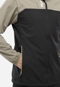 Veste softshell noire et beige. Caractéristiques : fermeture éclair à l'avant, panneaux contrastants et poignets élastiques. Comprend des poches latérales et une coupe ajustée.