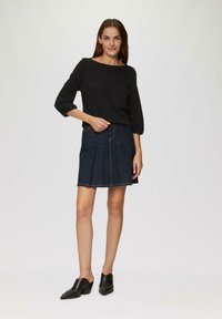 Zwarte langemouwenshirt met een bootcut halslijn, gecombineerd met een donkere denim geplooide rok. Zwarte hakken mules maken de outfit af.