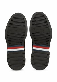 Suole delle scarpe in gomma nera con scanalature orizzontali; presenta strisce rosse, bianche e blu nella suola intermedia; logo inciso "TOMMY HILFIGER".