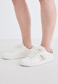 Hvide sneakers med dekorative metalliske accenter, med en glat overflade, rund tå, snørebånd foran og subtile glitrende striber.