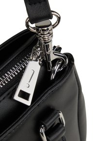 Sort syntetisk håndtaske med sølvfarvet lynlås, metalhardware og et mærkat med et udråbstegn. Glat tekstur.