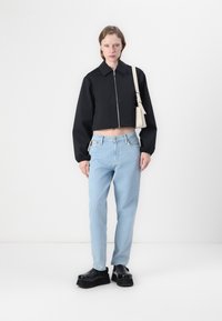 Mustapata must mungad na zipper yembuli, jinzi wembuli yimbili, na viatu vya majukwa ya mblack. Modeli anashikilia mfuko mweupe mdogo.