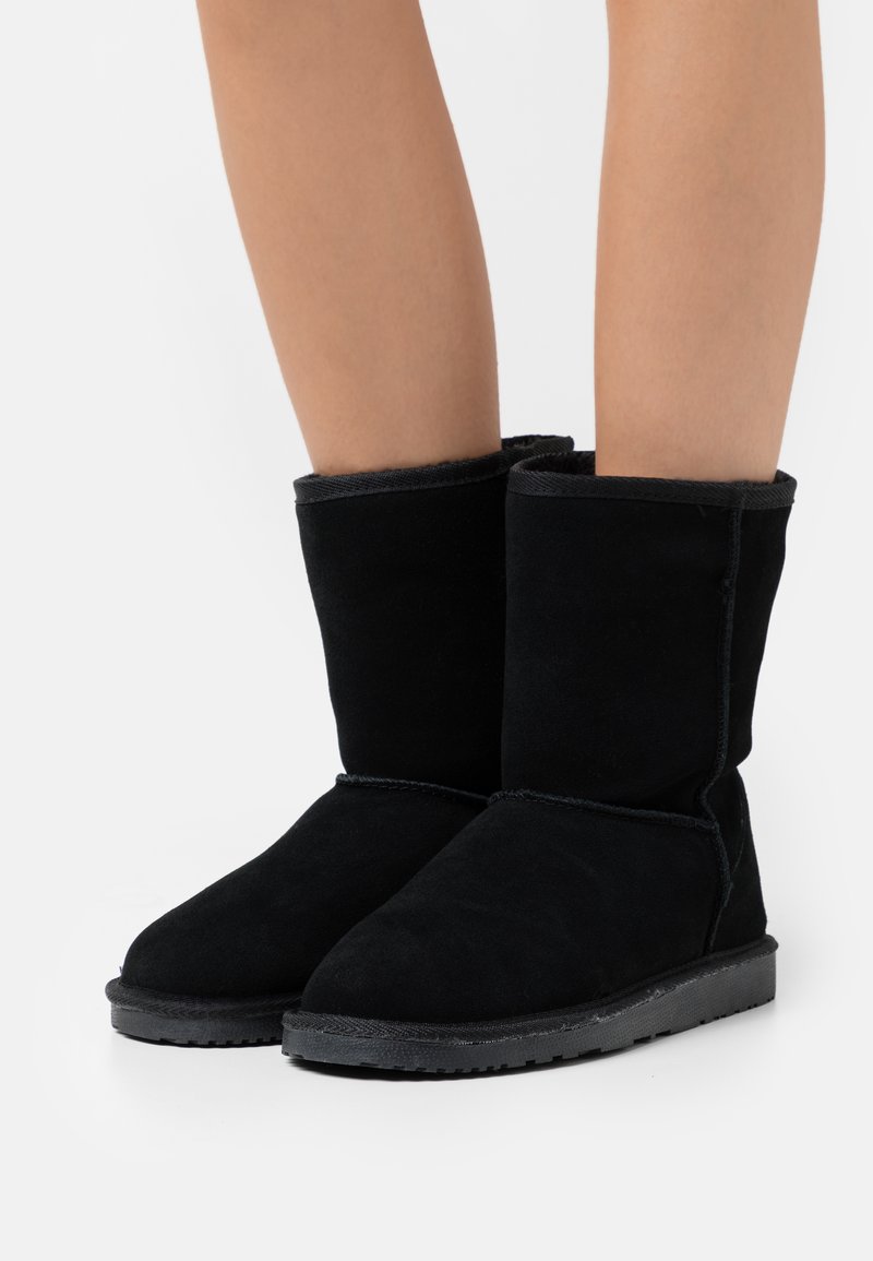 Black suede ankle boots with a rounded toe and a flat rubber sole. Features a soft inner lining and stitched detailing along the seams.