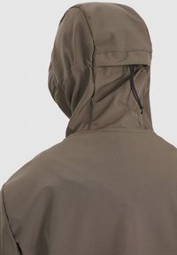 Personne portant une veste à capuche taupe vue de dos, dotée d’un cordon de serrage noir ajustable sur la capuche.