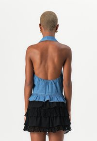 Denim halter top z odprtim hrbtom, ki ima nabran rob, združen z večplastno črno mini krilo z čipkastimi detajli.
