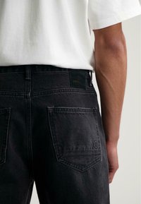 Czarne dżinsy z denimu o średnim stanie, z dwiema tylnymi kieszeniami i markową skórzaną naszywką na pasie. Szorstka faktura, casualowy design.