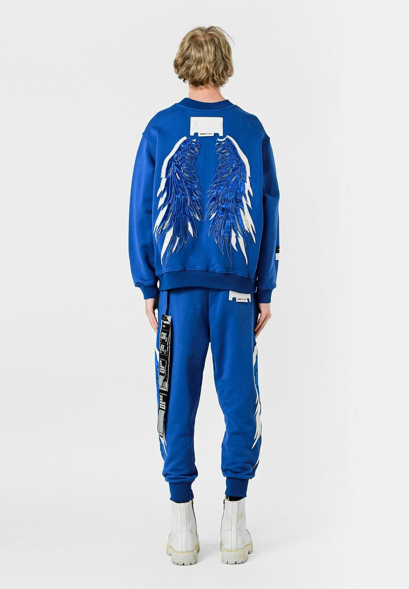 Conjunto de sudadera y pantalones azul, con diseños de alas blancas y azules en la espalda y los lados. Hecho de un tejido suave con puños acanalados.