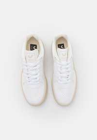 Hvide lædersneakers med perforeret design, flade hvide snører, brune gummisåler og et subtilt logo på tungen og siden.