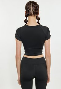Sort cropped atletisk top med korte raglanærmer, der har en glat tekstur og en tætsiddende silhuet, kombineret med sorte leggings.