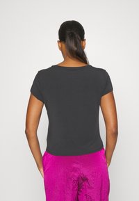Camiseta negra de manga corta con cuello redondo, de textura suave y forma ajustada, combinada con pantalones brillantes rosas. El fondo es totalmente blanco.