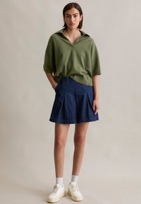 Zielony sweter z dzianiny o szerokim kołnierzu, zestawiony z ciemnoniebieską plisowaną spódnicą z denimu. Całość dopełniają białe trampki z kremowymi akcentami.