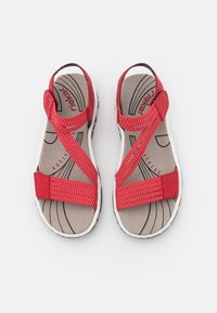 Sandales rouges avec des brides croisées, fabriquées en tissu tissé. La semelle intérieure grise présente un motif ondulé, tandis que la semelle extérieure blanche offre une adhérence texturée.