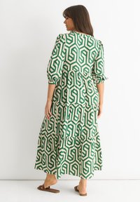 Maxi dress in green and beige geometric pattern, featuring puff sleeves, tiered ruffles, and a relaxed fit. Worn with brown flat sandals.
