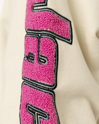 Krém színű szövet, amelyen nagy, bolyhos rózsaszín felirat található, fekete és kék szegéllyel az oldalán, texturált mintával.