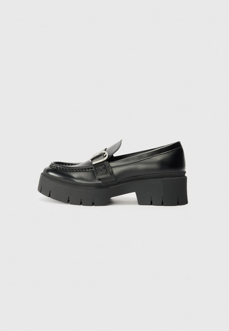 Sorte skinnloafers med en kraftig gummisåle. Har et spenneaksent og broderte detaljer langs overdelen. Flat hel.