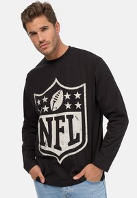 T-shirt a maniche lunghe nera con una grande grafica del logo NFL invecchiato, un pallone da football e stelle, realizzata in morbido cotone.