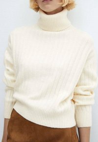 Maglione a collo alto color crema con texture a coste, maniche lunghe e vestibilità ampia, abbinato a una gonna in suede marrone.