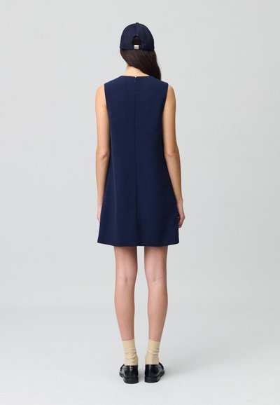 Vestido sin mangas azul marino de corte recto, con cremallera en la parte posterior y textura suave, combinado con zapatos negros y calcetines beige.
