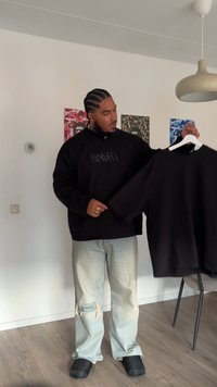 Felpa nera oversize con logo "HORATI" sul davanti, collo rotondo e spalle cadenti, tenuta da una persona su uno sfondo chiaro.