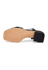 Schwarzer High Heel mit strukturiertem Absatz, ausgestattet mit einer nudefarbenen Gummisohle und einem klobigen Absatzdesign, das mit einem eleganten Riemen-Detail versehen ist.