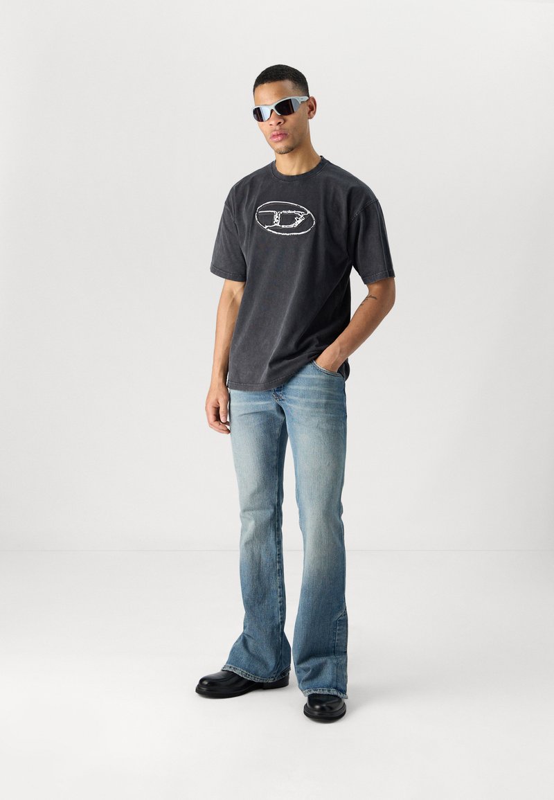 Schwarzes Grafik-T-Shirt, hellblaue Schlagjeans und schwarze Schuhe. Accessorized mit grauen Sonnenbrillen. Einfaches Design mit minimalen Details.