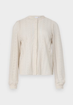 Õrna pitsist pluus kreemjashallide toonide kombinatsioonis, ümmarguse kaeluse, nööbiga esiotsa ja pikkade varrukatega, millel on kogutud mansetid. Detailne lillemuster üle kogu pluusi.