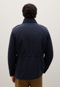 Giacca blu navy con collo alto, vita elasticizzata e polsini con bottoni. Dotata di spalline sulle spalle e realizzata in materiale liscio e resistente all'acqua.