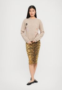 Maglione beige con ricami multicolore; gonna gialla con strisce di tigre nere; modello indossa ballerine nere; vista frontale su sfondo semplice.