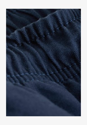 Granatowa tkanina o fakturze z marszczonym przeszyciem, ukazująca miękki i elastyczny materiał. Skupienie na elastycznym pasie.