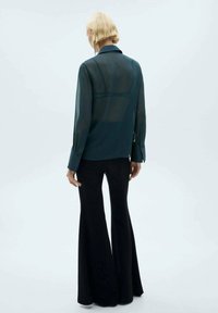 Transparent dark teal blouse with long sleeves, button cuffs, and a collar, paired with fitted black flared pants. Minimalistic styling.