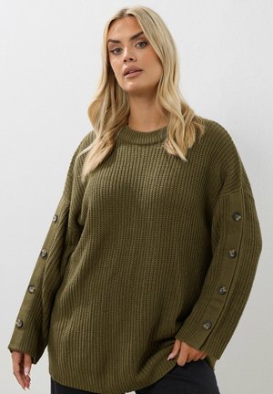 Knit sweater in olive green with a textured rib design, oversized fit, round neckline, and button accents along the sleeves.