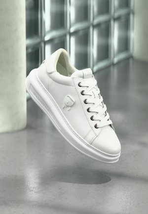 White leather sneaker featuring a round toe, lace-up design, metallic eyelets, and a textured sole. Embossed logo on the side.