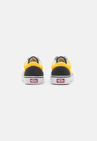 Gule og svarte lerrets sneakers med hvit såle, med en rød logo på hælen og kontrasterende sømmer.