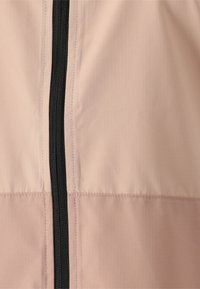 Vaaleanpunainen kangas, jossa on hienovarainen nauhamainen rakenne, musta vetoketju keskellä sulkemista varten. Saumojen yksityiskohdat näkyvät.