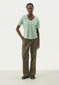 Grön kortärmad topp med V-ringning och blommönster, i kombination med löst sittande khakibyxor. Bärs med svarta sandaler.