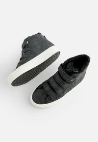 Scarpe alte nere con tre cinturini in velcro, tessuto testurizzato, suole in gomma bianca e interno morbido nero. Presentano un accento a forma di stella.