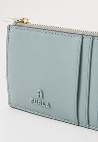 Light blue leather wallet with gold zipper and embossed logo. Features card slots and a smooth texture with neat stitching.