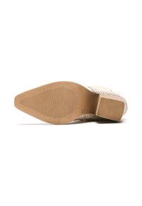 Zapato de tacón alto beige con un patrón texturizado, una abertura resistente en la parte delantera y una suela de goma texturizada marrón. Tacón plano en la parte trasera.