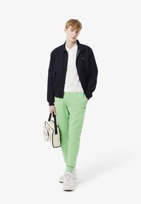 Marine bomberjakke, hvid polo, lysegrøn sweatpants og beige taske med sorte accenter. Sporty sneakers med teksturerede detaljer.