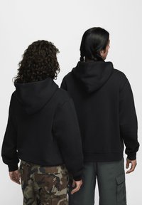 Μαύρα φούτερ με κουκούλα και κορδόνια, χαλαρή εφαρμογή και ριμπ μανσέτες. Το ένα συνδυάζεται με παντελόνια παραλλαγής, το άλλο με cargo σορτς σε ελιά πράσινο.