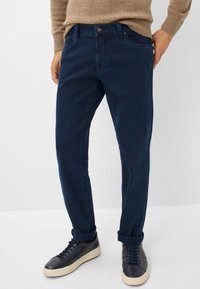 Pantalons en coton bleu marine, coupe droite, cinq poches et fermeture à bouton, associés à des baskets noires avec semelles claires.