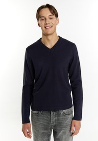 Marinblå stickad v-neck-tröja med lång ärm, med ett ribbat halsband och manschetter, parat med grå denimjeans.