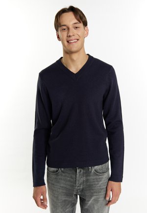 Marineblauwe gebreide V-hals trui met lange mouwen, met een geribde halslijn en manchetten, gecombineerd met grijze denim jeans.