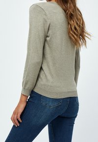 Jasnooliwkowy sweter z okrągłym dekoltem, ściągaczami przy mankietach i dopasowanym krojem, zestawiony z niebieskimi dżinsami. Tekstura wygląda na miękką i gładką.