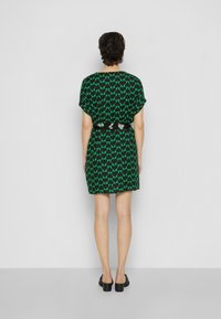 Abito verde e nero con motivo a cuore, maniche corte, vita cinchata e vestibilità comoda. Scarpe nere completano l'outfit.