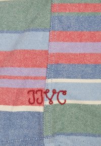 Meerling textiel met horizontale strepen in blauw, groen, rood en paars, met geborduurde tekst "JJYC" in rood garen.